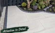 Large light-grey porcelain slabs with a dark gravel edge and a small tree in a planted bed.
