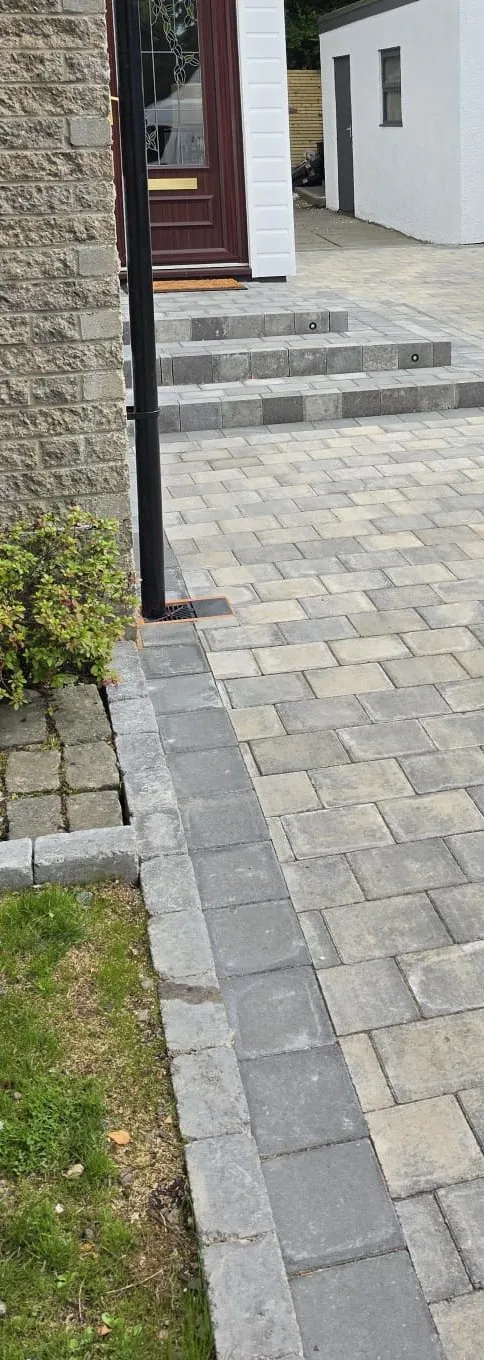 Grey block paving and new block steps leading to a burgundy front door, with a white garage beyond.
