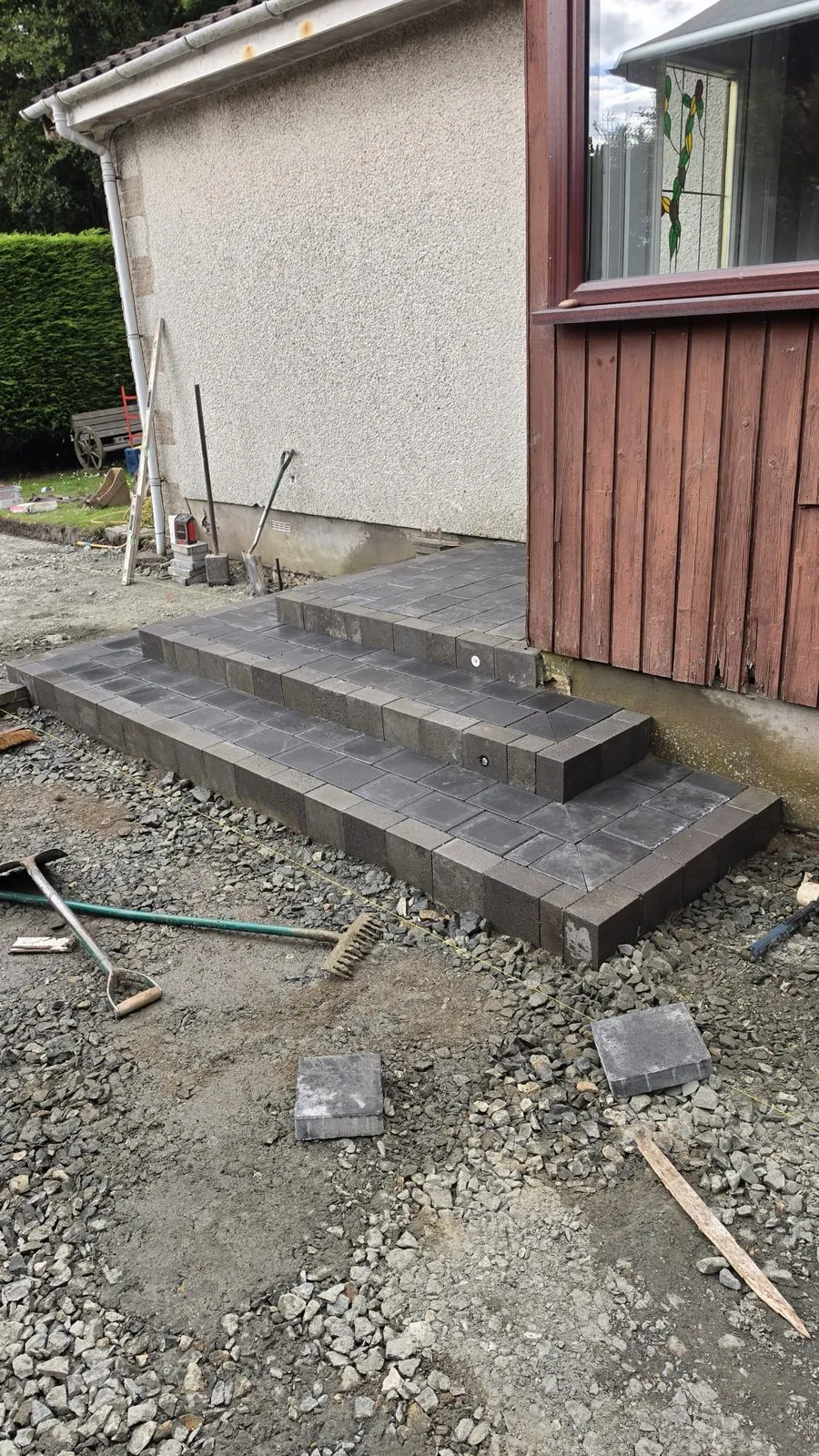New dark block steps built against a pebbledash wall, with gravel and tools still on the ground.