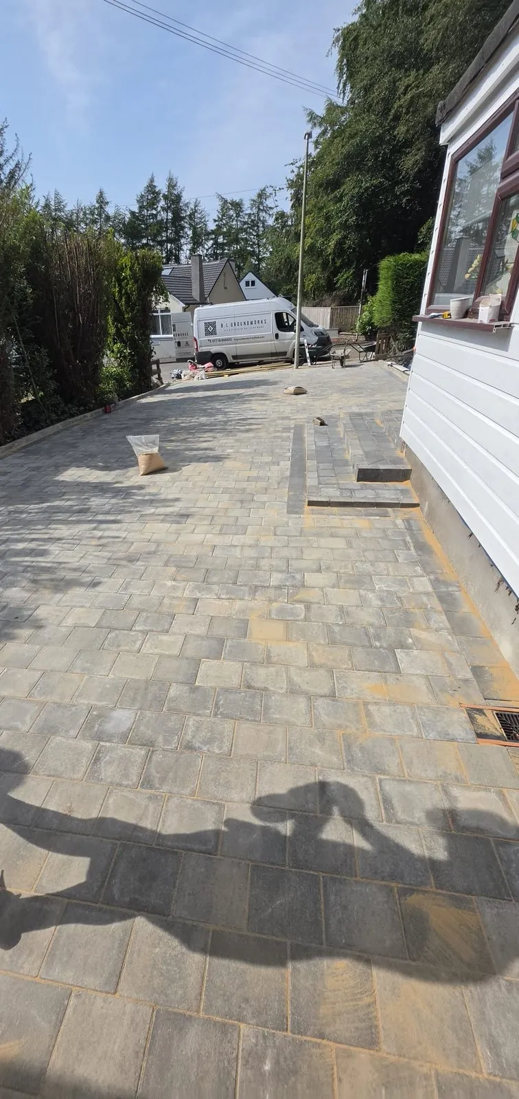A block-paved drive part finished beside a white wall, with the company van parked further up the plot.